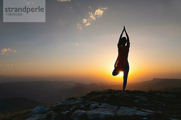 Silhouette einer jungen Frau in einer Baumpose im Freien in den Bergen beobachten den Sonnenuntergang  Yoga Balance in der Nähe der Klippe