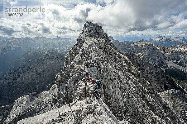 Bergsteigerin in einem mit Stahlseil gesicherten Klettersteig  schmaler felsiger Berggrat  Watzmann Überschreitung zur Watzmann Mittelspitze  Ausblick auf Bergpanorama mit Steinernes Meer  Nationalpark Berchtesgaden  Berchtesgadener Alpen  Bayern  Deutschland  Europa