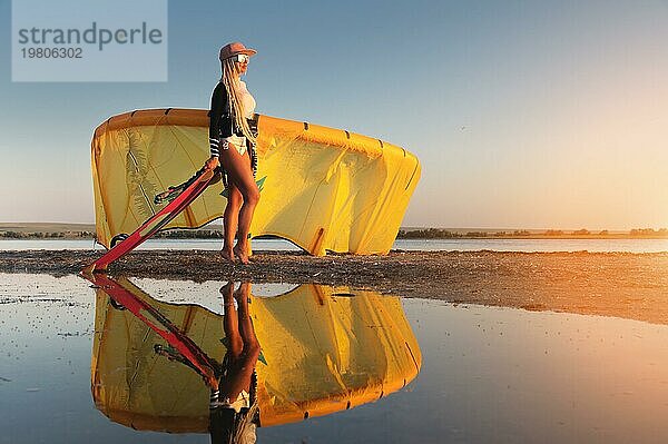 Sexy junge Frau steht mit einem Surfbrett auf einem Meer Strand mit Sand. Kiteboard Lehrer  Sonnenuntergang