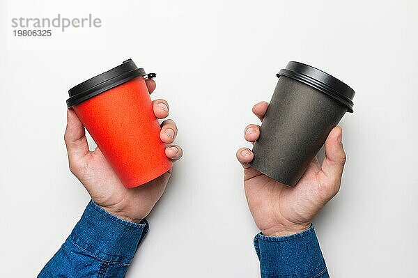 Nahaufnahme  männliche Hände halten zwei Pappbecher mit Kaffee auf weißem Hintergrund  Draufsicht