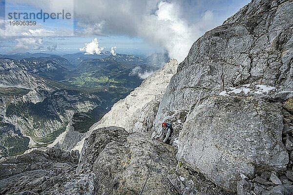 Bergsteigerin in einem mit Stahlseil gesicherten Klettersteig  steile felsige Bergflanke  Watzmann Überschreitung zur Watzmann Mittelspitze  Ausblick auf Bergpanorama  Nationalpark Berchtesgaden  Berchtesgadener Alpen  Bayern  Deutschland  Europa