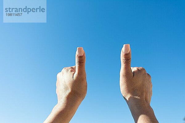 Frauenhände mit Daumen auf einem blauen Himmel Hintergrund