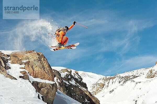 Ein professioneller Skifahrer springt von einer hohen Klippe gegen den blaün Himmel und hinterlässt eine Spur aus Pulverschnee in den Bergen. Foto von den Hängen des Berges Elbrus. Das Konzept des Extremsports und der Erholung in den Bergen im Winter. Kopieren Sie den Raum