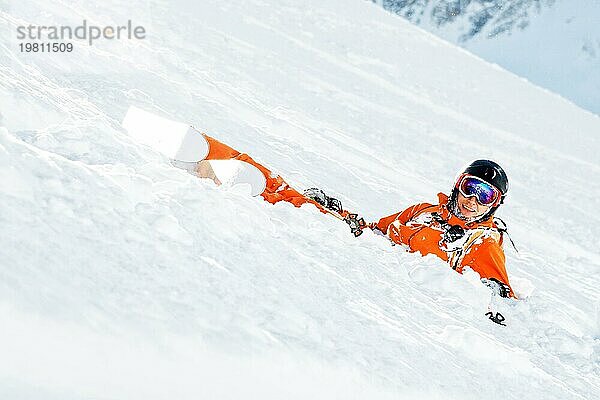 Ein Skifahrer in einem orangefarbenen Overall und mit einem Rucksack liegt nach einem Sturz glücklich im Schnee. Das Konzept der Erholung in den Bergen und des Skifahrens