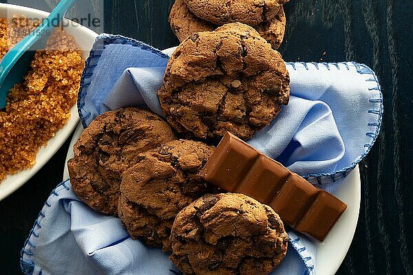 Chocolate Chip Cookies auf einem weißen Teller neben braunem Zucker und ein Stück Milchschokolade  Draufsicht Schokoladenkekse. Auflösung und hohe Qualität schönes Foto