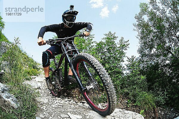 Ein junger Fahrer auf einem Fahrrad für Downhill steigt die Felsen im Wald hinunter