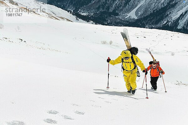 Zwei Ski Freerider klettern den Hang im Tiefschnee hinauf  die Ausrüstung auf dem Rücken am Rucksack befestigt. Das Konzept des Winter Extremsports