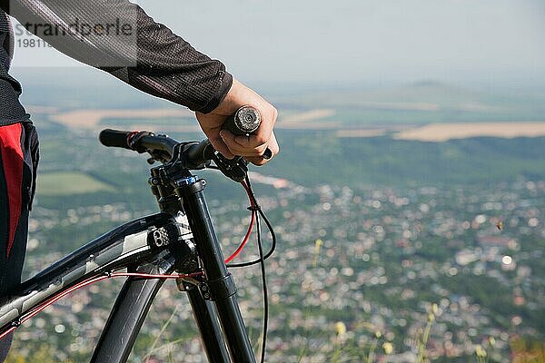 Nahaufnahme der Hand eines Fahrers am Lenker eines Mountainbikes mit geringer Tiefenschärfe vor dem Hintergrund der Stadt