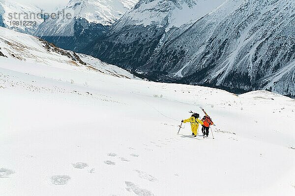 Zwei Ski Freerider klettern den Hang im Tiefschnee hinauf  die Ausrüstung auf dem Rücken am Rucksack befestigt. Das Konzept des Winter Extremsports