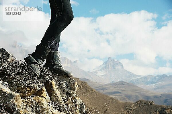 Nahaufnahme von weiblichen Füssen in Vintage Stiefeln stehen auf einem Felsen in den Bergen vor dem Hintergrund einer epischen Landschaft von Märchenfelsen und Wolken auf dem holoomed Himmel. Das Konzept der Entspannung in den Bergen