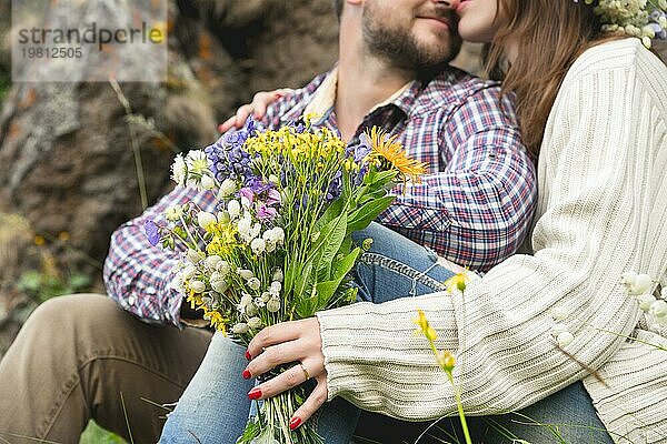 Nahaufnahme der Hände eines jungen Hipster Paares  das in der Natur spazieren geht und einen Strauß Wildblumen in den Händen hält