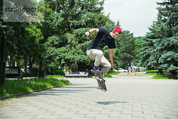 Langhaariger Skater Teenager in TShirt und Turnschuhmütze springt den Ollie vor dem Hintergrund eines stürmischen Himmels über der Stadt