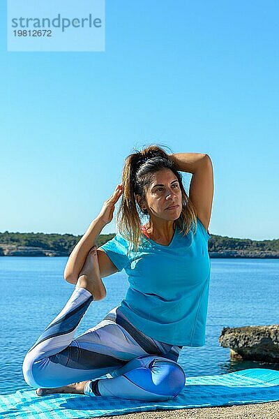 Fitnessfrau mittleren Alters im Freien vor dem Meer macht Yoga Stretching Übungen
