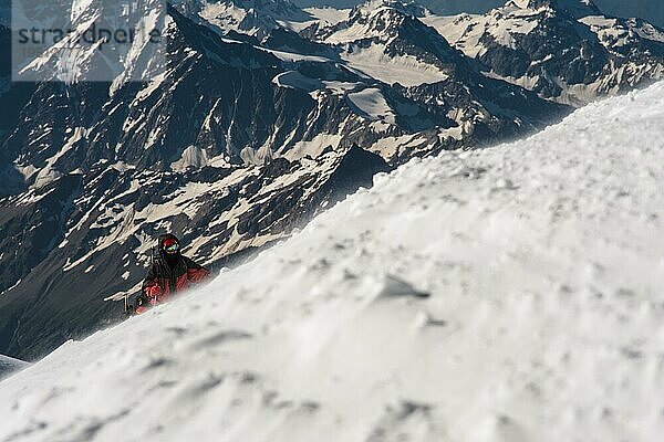 Der Bergsteiger erklimmt den schneebedeckten Gipfel vor dem Hintergrund der schneebedeckten Berge des Kaukasus  Das Konzept der Überwindung von Schwierigkeiten und der Erreichung des Ziels