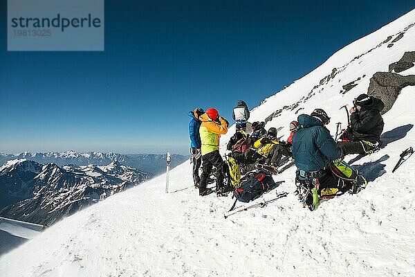 Vollständig ausgerüstete Profi Bergsteiger sitzen bei sonnigem Wetter auf einer verschneiten Piste. Das Konzept der kollektiven Erholung in den Bergen