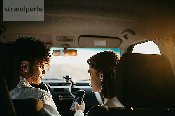 Schönes junges verliebtes Paar im Auto  das sich eine Wochenendreise auf einem Smartphone ansieht