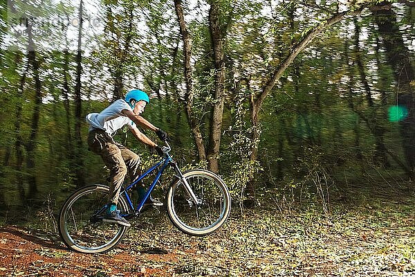 Ein junger Radfahrer mit Helm landet nach einem Sprung von einem hohen Kicker auf einem Waldradweg auf dem Fahrrad. Schießen mit langer Belichtung Verdrahtung