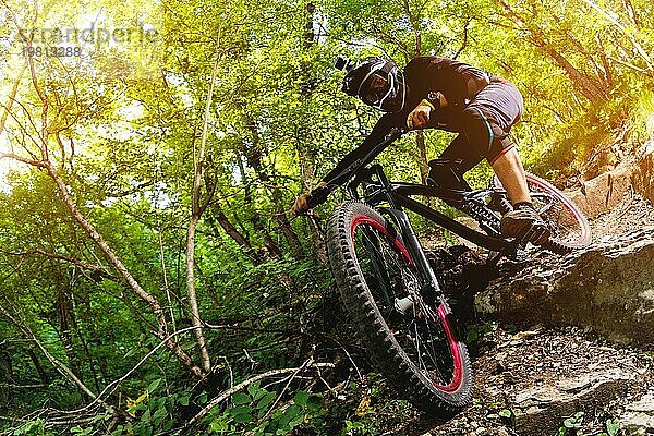 Ein junger Fahrer auf einem Fahrrad für Downhill steigt die Felsen im Wald hinunter