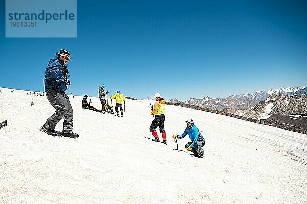 Training zum richtigen Abrutschen an einem Hang oder auf einem Gletscher mit Hilfe eines Eispickels. Ein junger Bergführer mit Bart erklärt seiner Gruppe  wie man das Abrutschen am Hang mit Hilfe eines Eispickels richtig bremst. Vorbereitung vor dem Aufstieg auf den Berggipfel