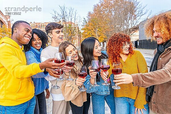 Multiethnische Freunde lächeln und stoßen mit Rotwein auf der Straße an