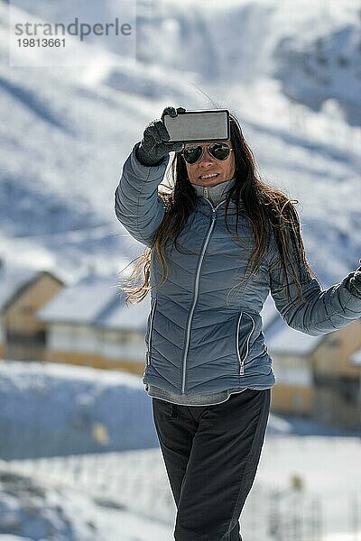 Eine Frau in Winterkleidung macht ein Selfie mit verschneiten Bergen im Blick