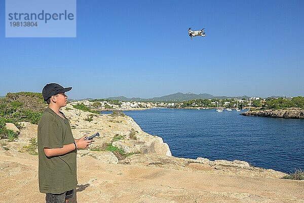 Glücklicher Teenager  fliegende Drohne an der Mittelmeerküste  gegen blauen Himmel an einem sonnigen Tag Spanien  Balearen