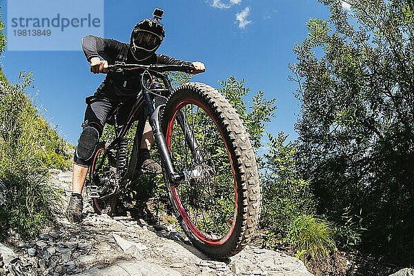 Ein junger Fahrer auf einem Fahrrad für Downhill steigt die Felsen im Wald hinunter