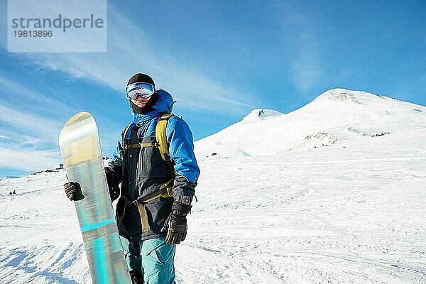 Ein professioneller Snowboarder steht mit seinem Snowboard vor der Kulisse des schlafenden Vulkans Elbrus. Nordkaukasus. Beschaffung für Werbung oder Plakat mit Copy Space. Konzept von Wintersport und Erholung