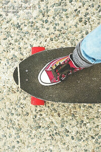 Detail Skateboard teilweise groß mit den Beinen einer Frau in Turnschuhen