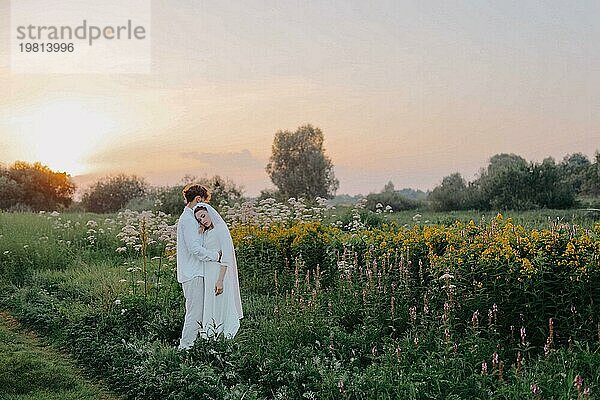 Verliebtes Brautpaar bei Sonnenuntergang auf dem Feld  die Braut und der Bräutigam in weißer Hochzeit