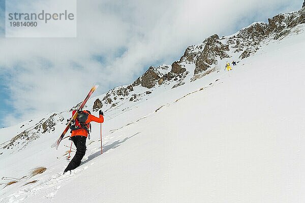 Der Ski Freerider klettert den Hang im Tiefschnee hinauf  wobei die Ausrüstung auf dem Rücken am Rucksack befestigt ist. Das Konzept des Winter Extremsports