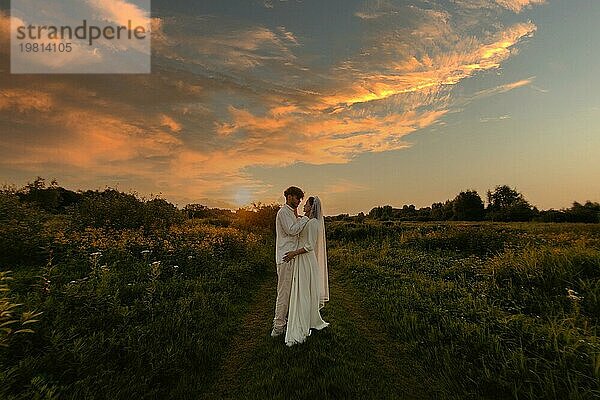 Verliebtes Brautpaar bei Sonnenuntergang auf dem Feld  die Braut und der Bräutigam in weißer Hochzeit