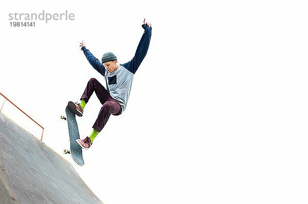 Der Teenager Skateboarder in der Mütze macht einen Trick mit einem Sprung auf der Rampe im Skatepark. Isolierte Skater und Rampe auf weißem Hintergrund