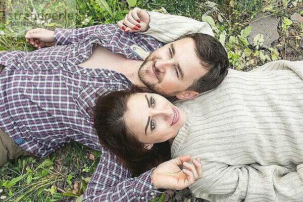 Ein verliebtes Hipster Paar liegt in einer Umarmung im Gras und streichelt sich gegenseitig