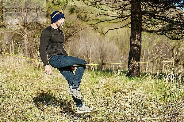 Ein Mann im Alter von auf der Slackline sitzend  das Gleichgewicht haltend und das Leben genießend