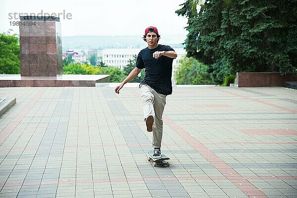 Ein Typ mit Mütze beschleunigt mit dem Fuß auf seinem Skateboard in einem Stadtpark