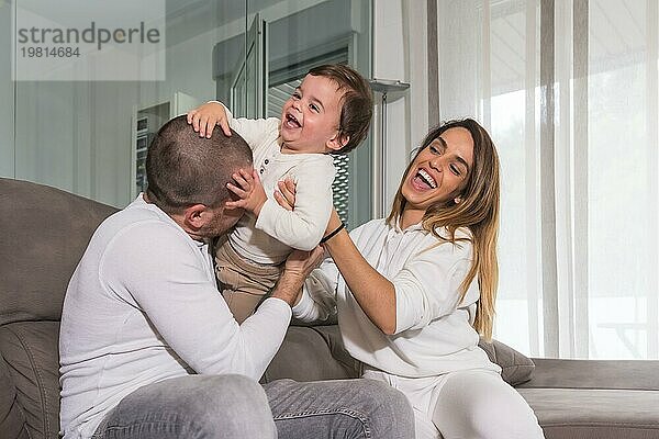 Glückliche Familie  die mit ihrem Baby lachend und spielend auf dem Sofa sitzt
