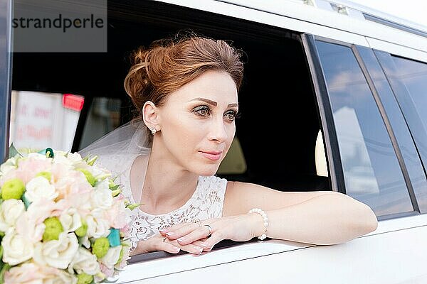 Nahaufnahme einer schönen Braut neben ihrem Brautstrauß im Fenster eines Hochzeitsautos. Das Konzept der Hochzeitsanmut