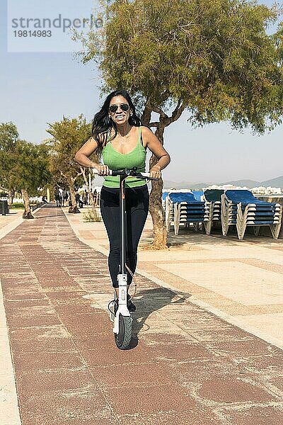 Junge Latina Frau mit Spaß mit elektrischen Roller am Strand