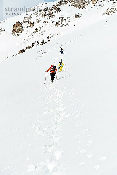 Zwei Ski Freerider klettern den Hang im Tiefschnee hinauf  die Ausrüstung auf dem Rücken am Rucksack befestigt. Das Konzept des Winter Extremsports