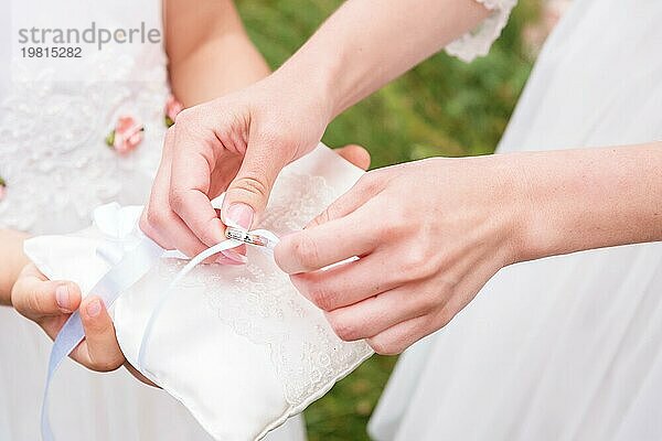 Hand Brautjungfer in weißem Kleid nimmt mit Pads Ringe. Kissen hält ein kleines Mädchen Brautjungfer