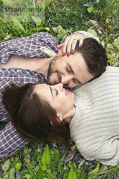 Ein verliebtes Hipster Paar liegt in einer Umarmung im Gras und streichelt sich gegenseitig
