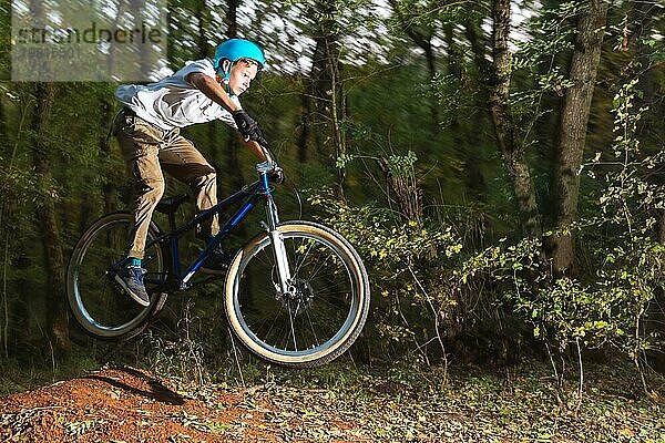 Ein junger Fahrer mit Helm fliegt auf einem Fahrrad  nachdem er von einem hohen Kicker auf einem Waldradweg gesprungen ist. Aufnahme mit Langzeitbelichtung Verdrahtung