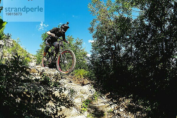 Ein junger Fahrer auf einem Fahrrad für Downhill steigt die Felsen im Wald hinunter