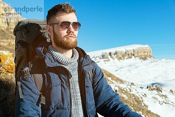 Ein Hipster Reisender mit Bart und Sonnenbrille in der Natur. Ein Mann wandern in den Bergen mit einem Rucksack und skandinavischen Wanderstöcke im Hintergrund eines Berges Elbrus Landschaft und blaün Himmel. Reisen Lifestyle Abenteuer Outdoor Erholung übertreffen