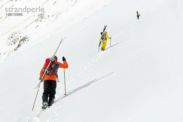 Zwei Ski Freerider klettern den Hang im Tiefschnee hinauf  die Ausrüstung auf dem Rücken am Rucksack befestigt. Das Konzept des Winter Extremsports