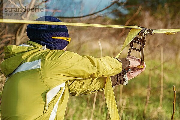 Nahaufnahme Hände eines Mannes  der die Slacklining Ausrüstung einstellt  bevor er verrückte Slacklining Tricks vorführt und auf einer Slackline in einem Park in der Natur läuft