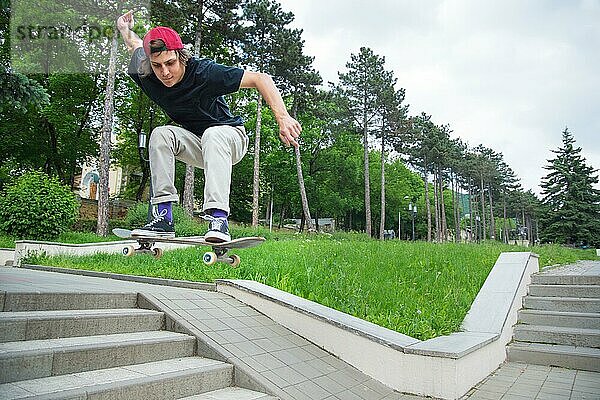 Langhaariger Skater Teenager in TShirt und Turnschuhmütze springt den Ollie vor dem Hintergrund eines stürmischen Himmels über der Stadt