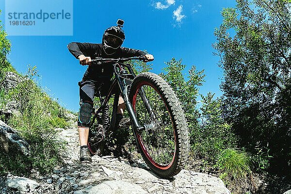 Ein junger Fahrer auf einem Fahrrad für Downhill steigt die Felsen im Wald hinunter