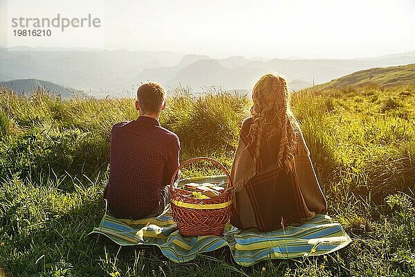 Blick von hinten. Junges Ehepaar beim Picknick im Freien bei Sonnenuntergang. Das Konzept einer glücklichen jungen Familie und Einheit mit der Natur
